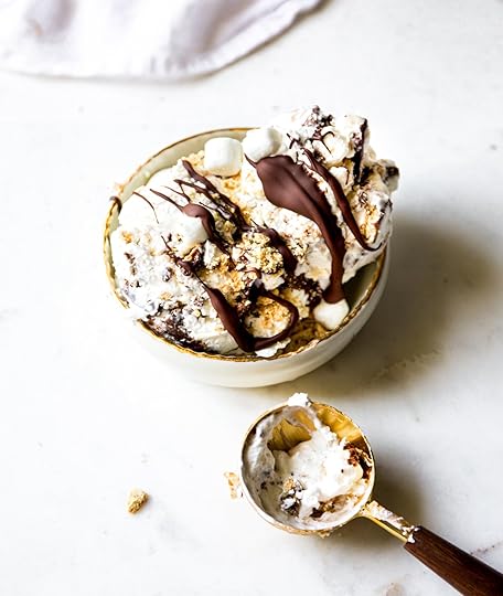 Overhead shot of a bowl of creamy homemade no-churn s'mores ice cream, generously drizzled with dark chocolate sauce and topped with crushed graham crackers and mini marshmallows. An ice cream scoop with a bit of ice cream sits below.