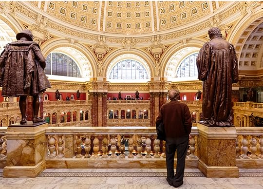 A visitor stands on the balcony of the Main Reading Room, flanked by two statues.