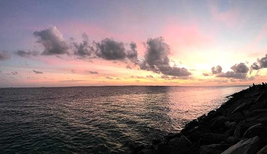 A seascape at dusk with waves in the foreground, and a reinforced revetment to the right.