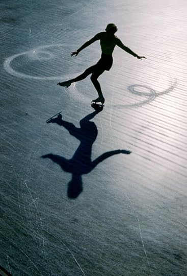 A figure skater with arms outstretched glides on textured ice, leaving swirls; silhouette and shadow stand out in soft cool light.