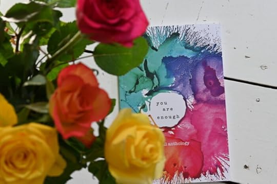 Anthology, 'You are Enough', with a cover of paint splashes, on white floor boards with yellow, red and orange roses in the foreground.