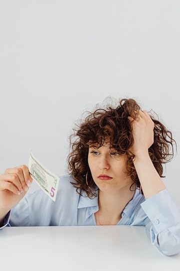 Woman looking frustrated while holding a five-dollar bill against a blank background symbolizing feeling trapped in scarcity and the call to wake up from the matrix.