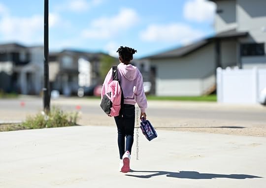 Photo of an elementary school child walking down the driveway, heading to school, wearing a pink hoodie, jeans and pink and white sneakers with a curly hairstyle in pigtails. She is carrying a pink and black adidas backpack, a lunch bag and wearing white sneakers. This photo is included in 