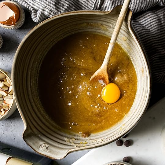 An egg yolk is dropped into a bowl of melted butter and brown sugar, ready to be mixed for almond chocolate chip cookies.