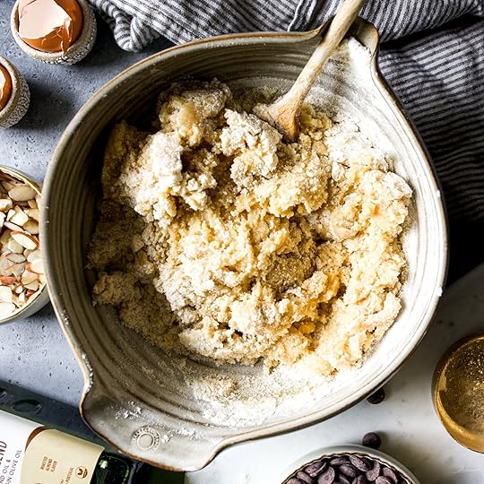 Partially mixed cookie dough with visible pockets of flour is stirred in a ceramic bowl, showing the final stages of combining ingredients.