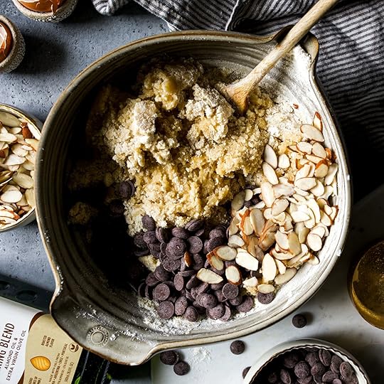 Chocolate chips and sliced almonds are placed on top of unmixed cookie dough in a ceramic bowl, ready to be folded in.