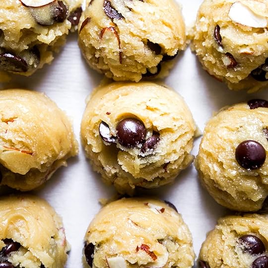 Perfectly portioned scoops of almond chocolate chip cookie dough, with visible chocolate chips and sliced almonds, arranged in a grid on a baking sheet.