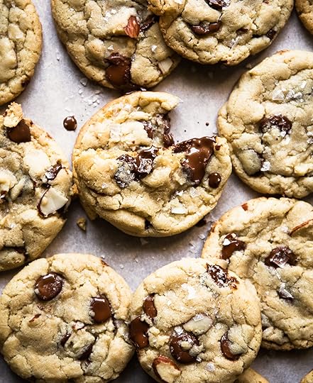 Chewy almond chocolate chip cookies with flaky sea salt on parchment paper, one cookie has a bite taken out of it revealing melted chocolate chips.