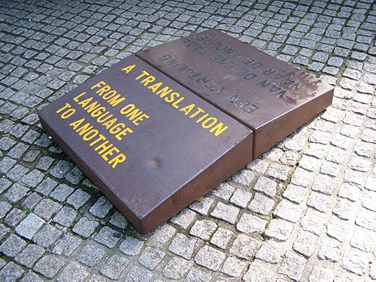 Het kunstwerk ‘Een vertaling van de ene taal naar de andere’ van Lawrence Weiner, 1996, op het Spui in Amsterdam. 3 paren van 2 stenen, met dezelfde tekst in verschillende talen, zoals Nederlands, Engels, Surinaams en Arabisch. Via Wikimedia Commons