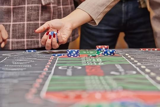 A person's hand with red-painted fingernails placing blue and white casino chips onto a marked casino table, with stacks of other chips visible, representing the act of betting and engagement in casino games.