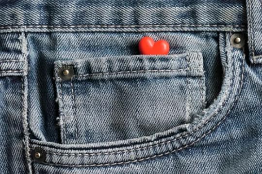 A small, red, heart-shaped charm is tucked into the front pocket of a pair of blue denim jeans.