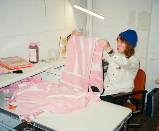 Cody is quilting a pink striped quilt and is wearing a blue hat