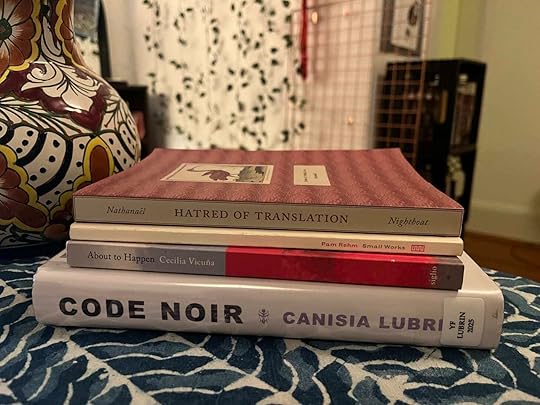 Photo of a stack of four books on a table with a table cloth. Next to them is a decorative jug and in the background a copper rack, fake ivy, and red yarn are (fuzzily) visible. The books' spines are facing towards the viewer. From bottom to top: Code Noir by Canisia Lubrin, About to Happen by Cecilia Vicuña, Small Works by Pam Rehm, and Hatred of Translation by Nathanaël.