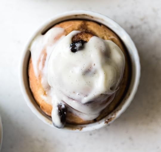 An overhead close up shot of a cinnamon roll covered in cream cheese glaze with lots of vanilla bean flecks.