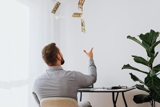 A guy sitting at his desk throwing money in the air symbolising EFT Tapping for Manifesting Money