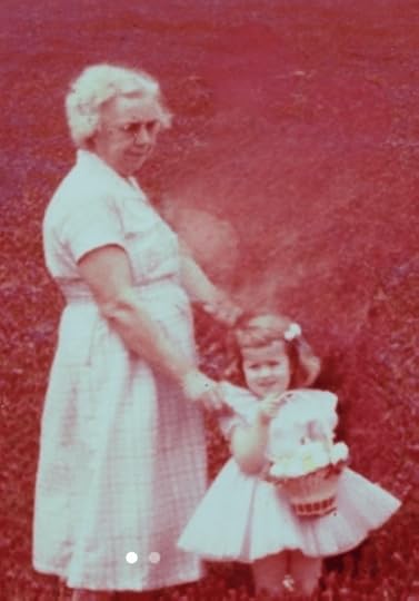 An older woman with gray hair and wearing a shirtwaist dress made of cotton, her left hand resting on the shoulder of an adorable (if I do say so myself!) little girl with a bow in her brown hair, wearing a yellow and gray organization dress trimmed with white lace and embellished with a poufy petticoat holding an overflowing Easter basket stand in a field of unending red clover