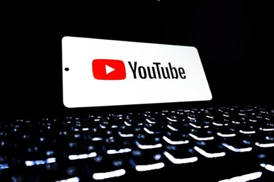 YouTube logo on a smartphone screen above a glowing computer keyboard in a dark setting