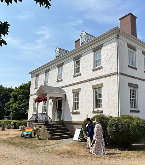 Two people in Regency attire walking past a white Georgian house.