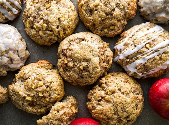 A close-up shot of several homemade apple cinnamon scones, some plain and some drizzled with a white glaze, on a dark baking sheet.