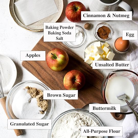 A flat lay of all the ingredients for a homemade apple cinnamon scones recipe, including apples, flour, butter, buttermilk, spices, and sugar.