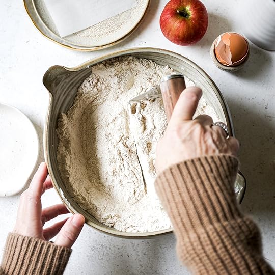 Hands using a pastry blender to cut cold butter into the dry ingredients for the apple scone dough.