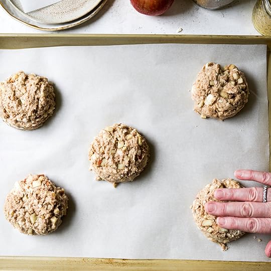 Hands shaping and flattening unbaked apple scone dough on a parchment-lined baking sheet.