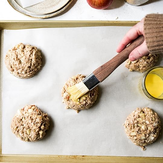 A hand using a pastry brush to apply an egg wash to unbaked scone dough on a baking sheet.