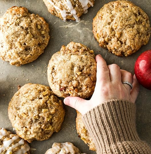 A hand in a cozy sweater reaching for a freshly baked apple cinnamon scone on a baking sheet.