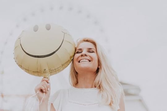 Smiling woman holding a yellow smiley face balloon, symbolizing the joy and calm that hand reflexology for stress can bring