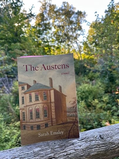 A copy of The Austens on a wooden fence with trees in the background