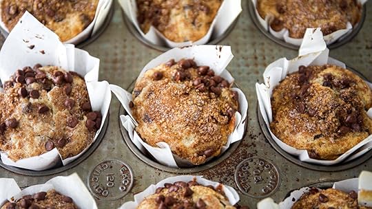 A full muffin tin of freshly baked bakery-style chocolate chip muffins with cinnamon streusel and chocolate chips on top. The muffins have tall, domed crowns and are in white paper liners.