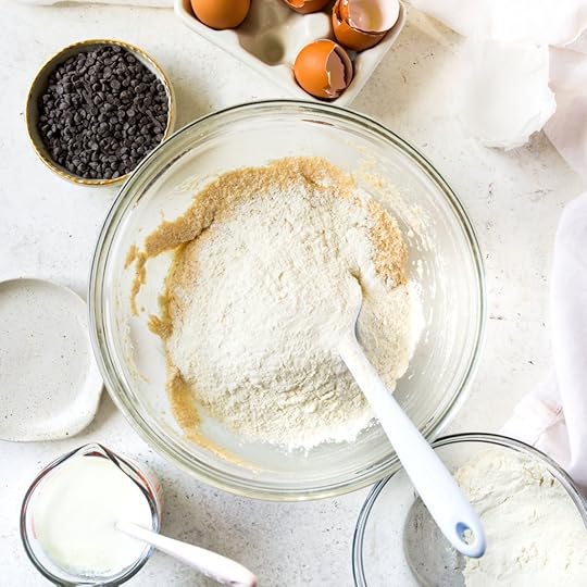 An overhead shot of a clear mixing bowl with wet ingredients and a pile of all-purpose flour waiting to be mixed.