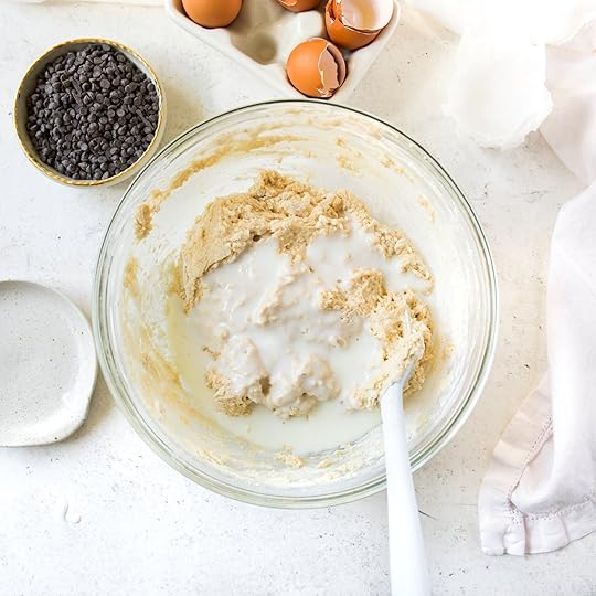 An overhead shot of a clear mixing bowl containing muffin batter with buttermilk being poured in, a key step for creating a moist crumb.