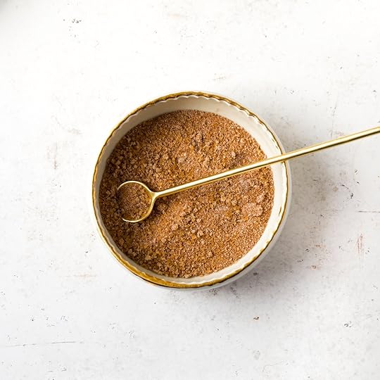  close-up of a small white bowl with a gold rim, containing a cinnamon brown sugar streusel topping and a gold spoon.