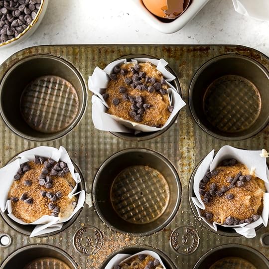 An overhead shot of a vintage muffin tin with three cups filled with chocolate chip muffin batter. The batter is topped with a cinnamon brown sugar streusel and more mini chocolate chips.