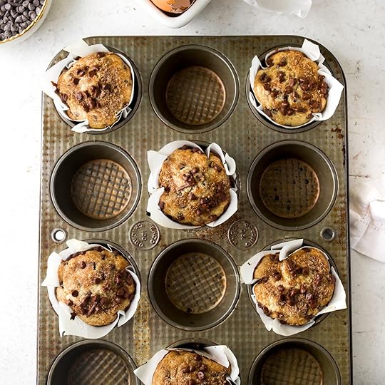 An overhead shot of a vintage muffin tin with several cups of baked bakery-style chocolate chip muffins and several empty cups. The muffins have tall crowns with a cinnamon brown sugar streusel and chocolate chips on top.