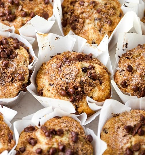 An overhead view of a fresh batch of bakery-style chocolate chip muffins with cinnamon brown sugar streusel and chocolate chips. The muffins have tall, domed crowns and are in white paper liners.