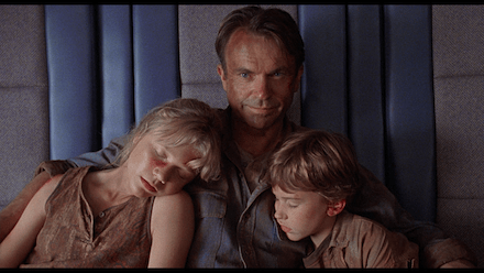 Closing scene of Jurassic Park showing Alan Grant with the two children asleep beside him in a helicopter, symbolizing his completed character arc from reluctance to protectiveness.