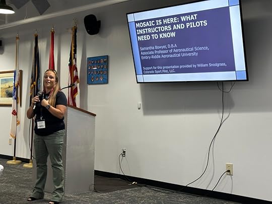 ERAU professor Samantha Bowyer outlined the changes brought into reality by the passing of MOSAIC for pilots and aircraft certification. She stands in front of a podium with a presentation displaying slides on the wall in the background.