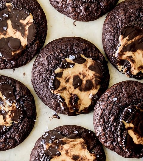 Overhead shot of rich double chocolate peanut butter cup cookies with glossy melted dark chocolate and peanut butter centers, sprinkled with sea salt on a parchment paper background.
