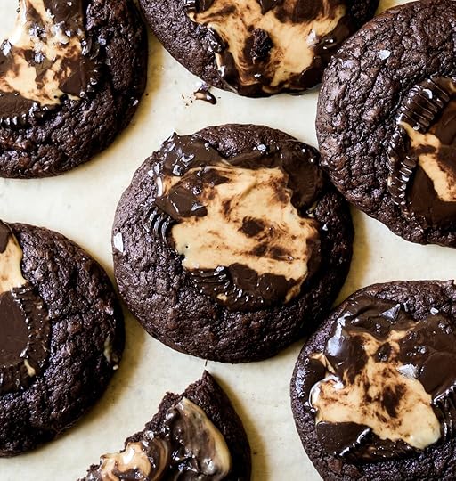 Close-up overhead image of freshly baked double chocolate cookies with crinkled edges and melted peanut butter cup swirls, sprinkled with sea salt on parchment paper.