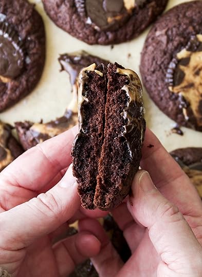 A hand holding a fudgy double chocolate peanut butter cup cookie split in half, showcasing the thick, soft, chewy interior and the melted peanut butter center.