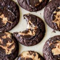 Chewy gooey chocolate peanut butter cup cookies with melted peanut butter centers and a sprinkle of sea salt on a parchment-lined baking sheet, one cookie has a bite taken out of it.