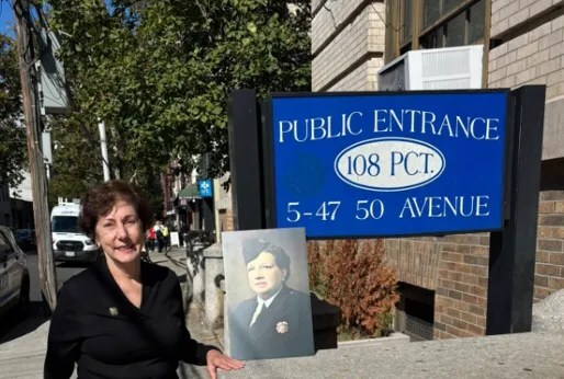 A woman stands outside by a blue sign reading 'PUBLIC ENTRANCE 108 PCT. 5-47 50 AVENUE,' holding a man's portrait. Trees, brick building.