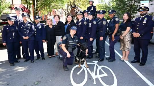 A group of police, some uniformed and some plainclothes, pose with a police dog. A mounted officer and bike lane symbol are visible.