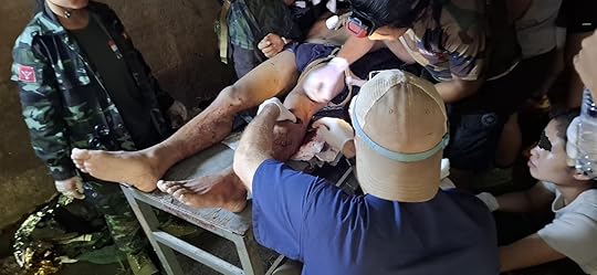 Medical personnel treating a severely injured leg in a dimly lit environment, surrounded by supportive individuals during an emergency situation.