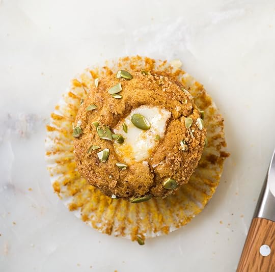 Overhead shot of a whole Pumpkin Cream Cheese Muffin, nestled in its paper liner, showcasing the streusel topping, green pepitas, and a creamy white cream cheese swirl.