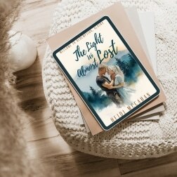 An e-reader with the picture of an ebook called The Light We Almost Lost by Heidi McCahan. The e-reader is stacked on top of a beige notebook on an ottoman with a cream colored knitted cover. There's a hardwood floor in the background.