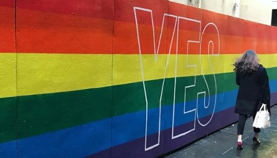 A woman walking past a rainbow wall with “YES” on it. You can choose to see the dark or seek the light.