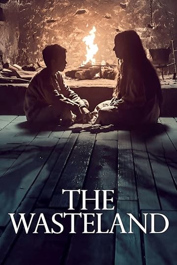 The Wasteland movie poster. A mother and son sit cross-legged and facing one another on bare floorboards of their cabin home in front of the open fire.